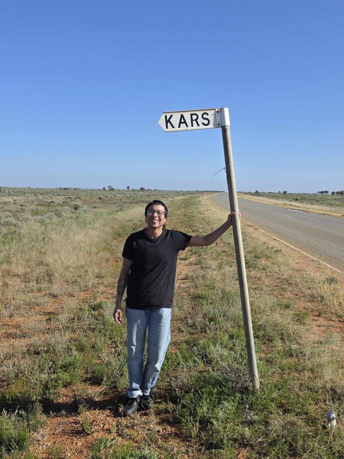 Kars standing under a roadside KARS sign.